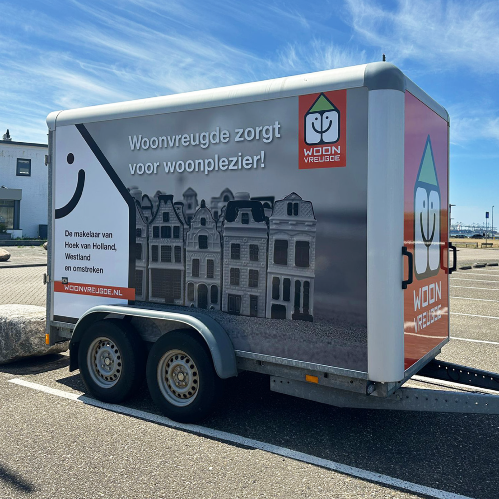 Zijaanzicht van een aanhanger met een opvallende reclamewrap, voorzien van een logo, quote, foto en website.