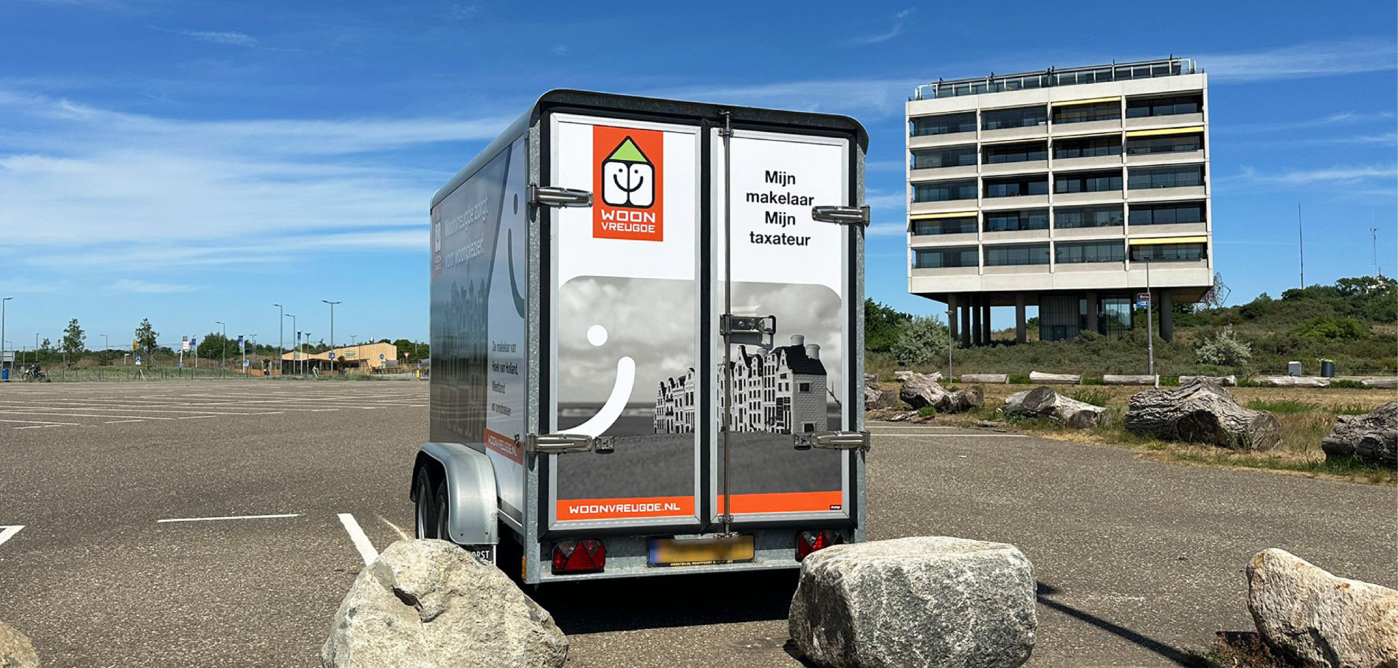 Achteraanzicht van een aanhanger met een opvallende reclamewrap, voorzien van een logo, quote, foto en website.