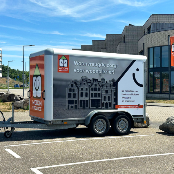 Zijaanzicht van een aanhanger met een opvallende reclamewrap, voorzien van een logo, quote, foto en website.