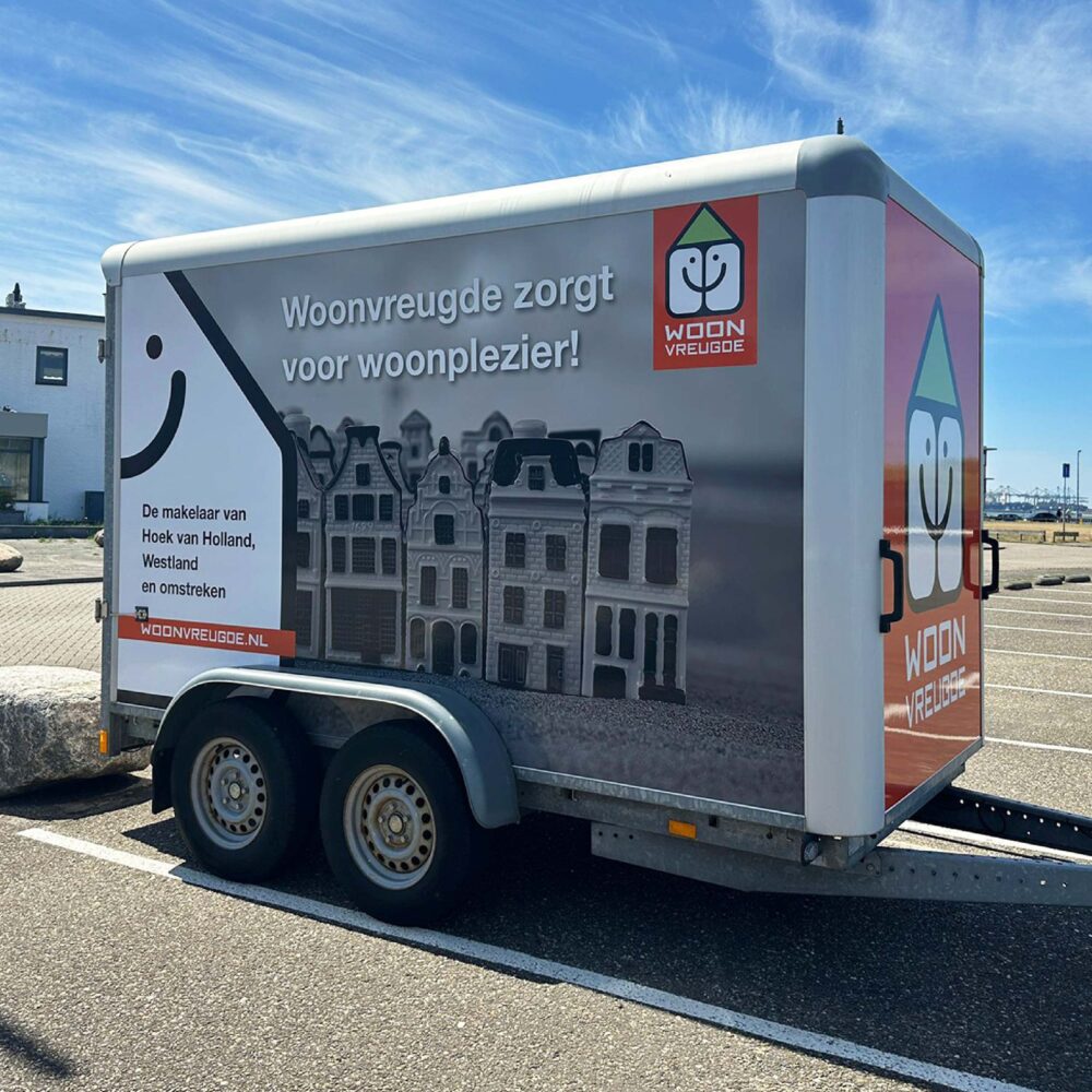Zijaanzicht van een aanhanger met een opvallende reclamewrap, voorzien van een logo, quote, foto en website.
