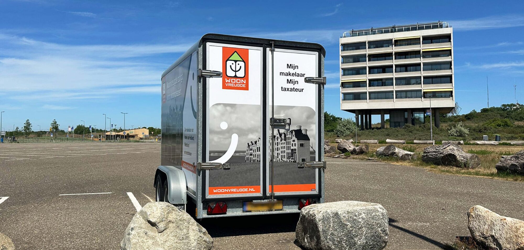 Achterkant van een aanhanger met een opvallende reclamewrap, voorzien van een logo, quote, foto en website.